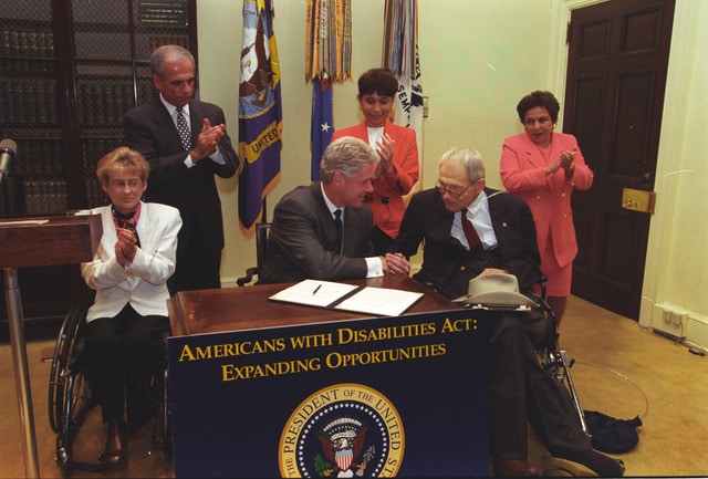 President Clinton signing a memorandum on outreach actions to increase employment of adults with disabilities. The ceremony commemorates the eighth anniversary of the Americans with Disabilities Act of 1990 (ADA).